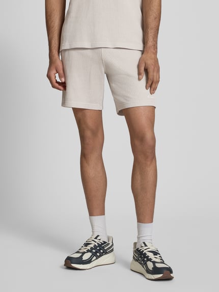 Männermodel trägt Shorts mit Strukturmuster und elastischem Bund von CHAMPION, Baumwoll-Mix, helles Beige, Regular Fit, Nahaufnahme Oberschenkel, Ganzkörperansicht von vorne.