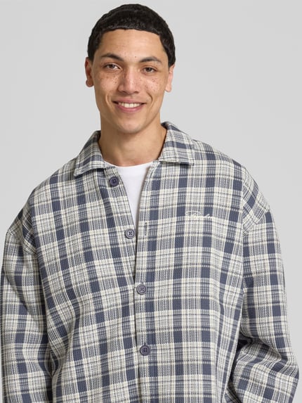 Männermodel trägt Relaxed Fit Freizeithemd mit Kentkragen und Label-Stitching von Pegador mit Strukturmuster, Nahaufnahme Oberkörper.