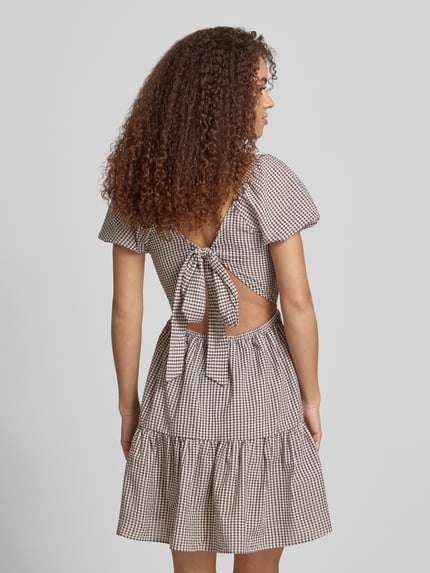 Frauenmodel trägt Knielanges Kleid mit Karree-Ausschnitt Modell 'ELIZA' von Noisy May im Material-Mix, A-Linie, kariertes Muster, Rückenansicht.