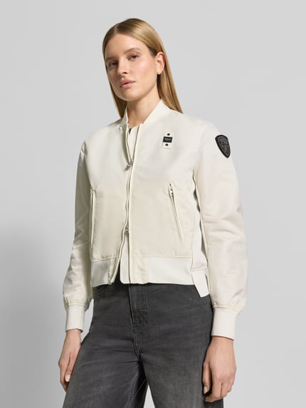 Frauenmodel trägt Bomberjacke mit Reißverschlusstaschen Modell 'LAURIE' von Blauer Usa in Creme mit Label-Patches, Nahaufnahme Oberkörper. Lose Passform mit gerippten Abschlüssen, Stehkragen und Zweiwege-Reißverschluss.