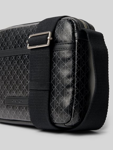 Produktfoto, Handtasche mit Logo-Muster und Schulterriemen von CK Calvin Klein, Herren, Hauptfach mit Reißverschluss, Label-Detail, verstellbarer Schulterriemen, Maße 22x16x5 cm, Schulterriemenlänge 106 cm, schwarze Textur mit silbergrauen Mustern.