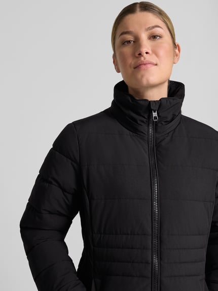 Frauenmodel trägt schwarze Jacke mit abnehmbarer Kapuze Modell 'ECLIPSE' von NAUTGÅRD, glatte Textur, Nahaufnahme Oberkörper. Gerader Schnitt, Zweiwege-Reißverschluss, Label-Patch, seitliche Eingrifftaschen mit Druckknopfverschluss, gestrickte Ärmelabschlüsse, Größe S: Rückenlänge 79 cm, Schulterbreite 38 cm, Brustweite 48 cm, Ärmellänge 62 cm.