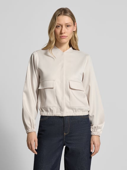 Frauenmodel trägt Bomberjacke aus Satin mit Pattentaschen von monari in Beige mit elastischen Abschlüssen, Ganzkörperansicht von vorne.