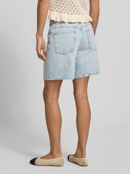 Modelka nosi szorty jeansowe z wpuszczanymi kieszeniami Jeansshorts mit Eingrifftaschen od REVIEW, krój regular fit, czysta bawełna, szerokość w rozmiarze S 39 cm, długość wewnętrzna nogawki 17 cm, zapięcie na guzik i zamek błyskawiczny, jasnoniebieski kolor, tekstura denimu, widok całej sylwetki od tyłu.
