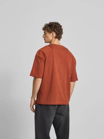 Männermodel trägt T-Shirt mit verstärktem Schultern von Dsquared2 in Rostrot, reine Baumwolle, Loose Fit, Rückansicht Ganzkörperansicht.