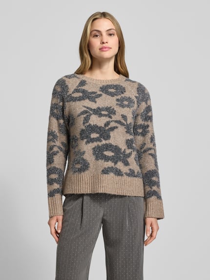 Frauenmodel trägt Strickpullover mit gerippten Abschlüssen Modell 'PANTEA' von FREE/QUENT in Beige mit anthrazitfarbenem Blumenmuster, lockerer Schnitt, Rundhalsausschnitt, weiche Textur, Ganzkörperansicht von vorne.