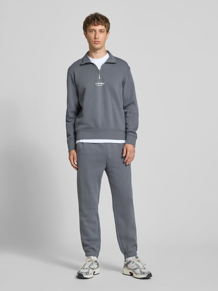 Männermodel trägt Regular Fit Sweatshirt aus Baumwoll-Mix Modell 'Soho' von JACK & JONES in Grau mit Logo-Print, Ganzkörperansicht von vorne. Rückenlänge bei Größe M: 67 cm, Ärmellänge bei Größe M: 66 cm, elastische Abschlüsse, Troyer-Kragen.
