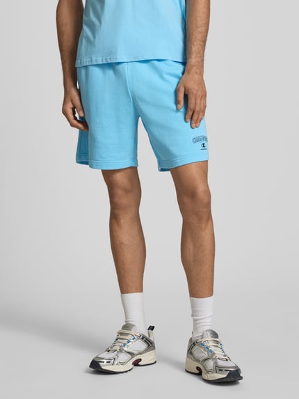 Männermodel trägt Sweatshorts mit Logo und elastischem Bund von CHAMPION in Hellblau, Baumwoll-Mix, Regular Fit, Nahaufnahme Oberkörper bis Knie.
