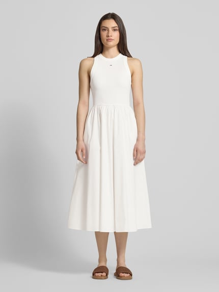 Frauenmodel trägt Midikleid aus reiner Baumwolle von Tommy Jeans in Unifarbe, A-Linie, ärmellos, Midi-Länge, Rundhals, Ganzkörperansicht von vorne.