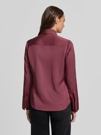 Frauenmodel trägt Slim Fit Bluse aus Satin Modell 'IDEALE' von MANGO in Dunkelrot mit Hemdblusenkragen und Knopfleiste, glatte Textur, Ganzkörperansicht Rückansicht.