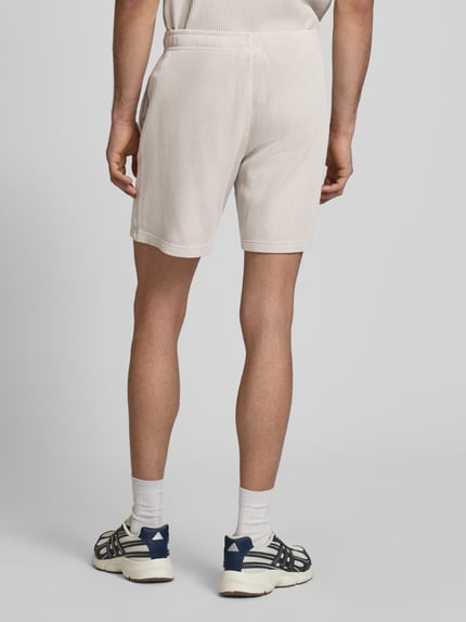 Männermodel trägt Shorts mit Strukturmuster und elastischem Bund von CHAMPION in Beige, Baumwoll-Mix, Ganzkörperansicht Rückansicht.