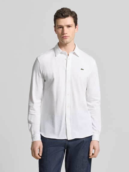 Männermodel trägt Slim Fit Freizeithemd aus reiner Baumwolle von Lacoste in Weiß, Optik: Unifarben, Logo-Stitching, Ganzkörperansicht von vorne.