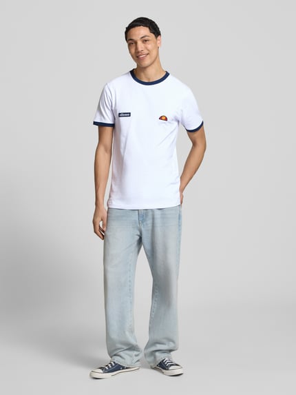 Männermodel trägt Herren T-Shirt mit Logo- und Label-Patch Modell 'RINGETTO' von Ellesse aus Reine Baumwolle, Gerader-Schnitt, Rundhalsausschnitt, Rücklänge bei Größe M 72 cm, weiße Grundfarbe mit dunkelblauen Details, Ganzkörperansicht von vorne.