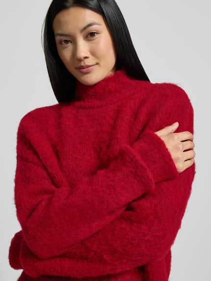 Frauenmodel trägt Strickpullover mit Stehkragen und überschnittenen Schultern von Milano Italy, roter Material-Mix mit Mohair-Anteil, Nahaufnahme Oberkörper.