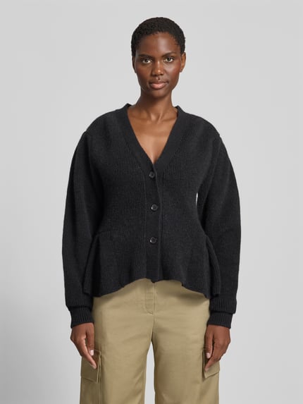 Frauenmodel trägt schwarzen Relaxed Fit Cardigan aus Alpaka-Mix von ROTATE mit Strick-Optik, Volant-Saum und Knopfleiste, Ganzkörperansicht von vorne, Rückenlänge 56 cm bei Größe S, elastischer Woll-Anteil.