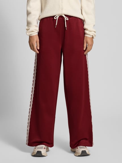 Frauenmodel trägt Sweathose mit Spitzenbesatz Modell 'Kael' von OH APRIL, weites Bein, bordeauxrot, elastischer Bund, Nahaufnahme Unterkörper.