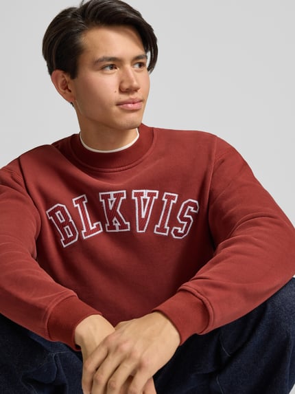 Männermodel trägt Sweatshirt mit Logo und Rundhalsausschnitt von BLKVIS in Dunkelrot aus Baumwolle, Relaxed Fit, Nahaufnahme Oberkörper.