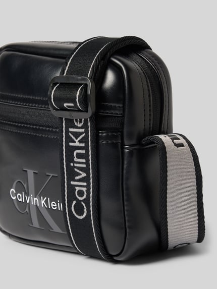Produktfoto, schwarze Herren Umhängetasche mit Logo-Prägung von CK Calvin Klein, dezente Glanzoptik und Stoffriemen auf grauem Hintergrund
