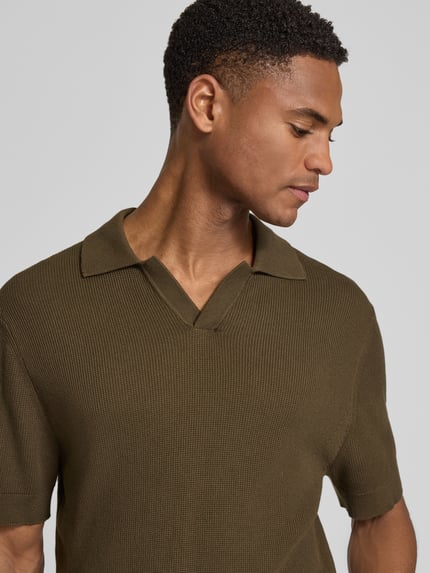 Männermodel trägt Regular Fit Strick-Poloshirt mit Strukturmuster Modell 'MOSVIK' von Casual Friday in Oliv mit V-Ausschnitt, Nahaufnahme Oberkörper.