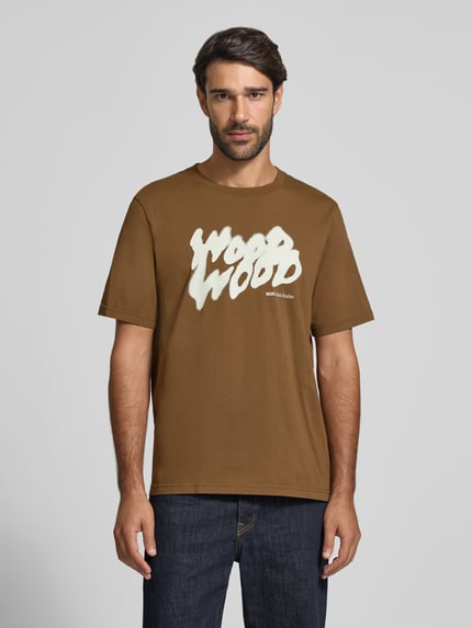 Männermodel trägt T-Shirt mit Label-Print Modell 'Bobby' von Wood Wood in Braun mit Rundhalsausschnitt, Regular Fit, Ganzkörperansicht von vorne.