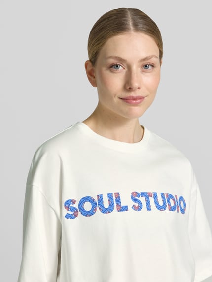 Kobiece modelka nosi Cropped Boxy Fit T-Shirt mit Label-Print von Smith and Soul, czysta bawełna, krój boxy fit, krótki fason, nadruk z logo, okrągły dekolt, długość tyłu w rozmiarze S: 48 cm, jasny kolor, prosty fason, gładka faktura, zbliżenie górnej części ciała