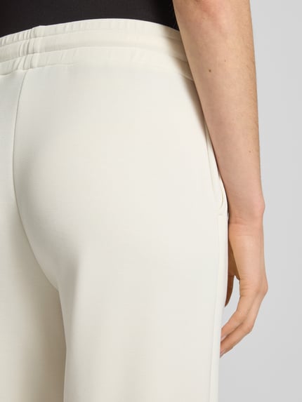 Frauenmodel trägt Sweatpants mit Label-Applikation Modell 'Talila' von JOOP! in Creme, elastischer Material-Mix, Detailaufnahme Rückansicht.