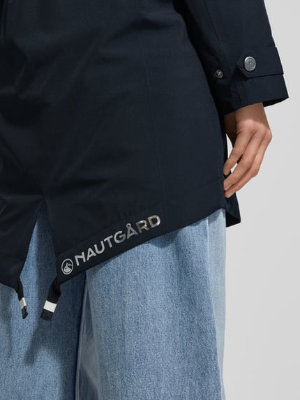 Kobiece model nosi Kurtka z patkami przy mankietach od NAUTGÅRD, krój regular fit, kolor granatowy, detaliczny widok dolnej części, zbliżenie. Długość tyłu w rozmiarze S: 90 cm, szerokość ramion w rozmiarze S: 45 cm, szerokość klatki piersiowej w rozmiarze S: 51 cm, długość rękawów w rozmiarze S: 62 cm.