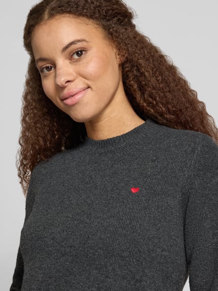 Kobiece modelka nosi Slim Fit Strickpullover aus elastischem Material-Mix od REVIEW, elastyczna mieszanka materiałów, krój slim fit, wyhaftowany motyw, prążkowane wykończenia, długość tyłu w rozmiarze S: 51 cm, długość rękawów w rozmiarze S: 61 cm, zbliżenie na górną część ciała.