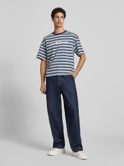 Männermodel trägt Regular Fit T-Shirt mit Logo-Stitching von KARL KANI, gestreift in Blau und Weiß, Reine Baumwolle, Ganzkörperansicht von vorne.