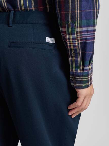 Männermodel trägt Wide Fit Bundfaltenhose aus reiner Baumwolle von Tommy Hilfiger in Optik: Unifarben mit Label-Stitching-Applikation, Detailaufnahme Rückansicht.