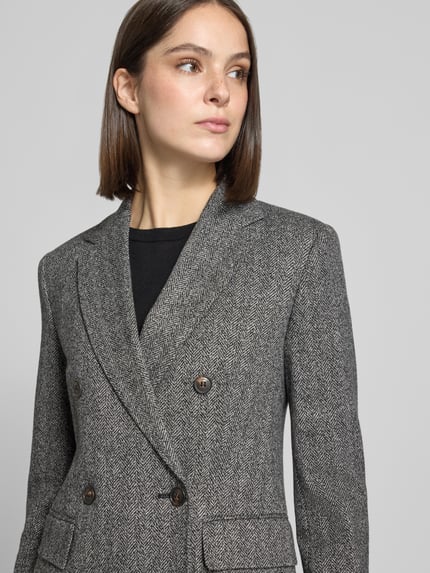 Frauenmodel trägt Regular Fit Kurzblazer mit doppelreihiger Knopfleiste von MAX MARA STUDIO aus Viskose-Baumwoll-Mix mit Fischgrätenmuster, Nahaufnahme Oberkörper.