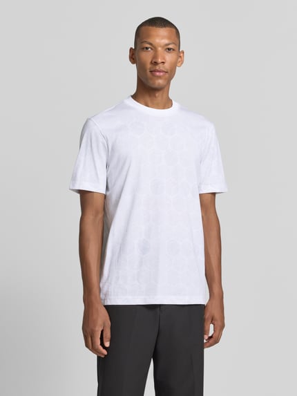 Männermodel trägt Regular Fit T-Shirt aus reiner Baumwolle von BOSS für BOSS Green in Weiß mit dezent gemusterten Flächen, Ganzkörperansicht von vorne.