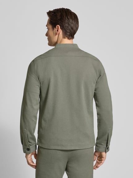 Męski model nosi Slim Fit Jacke mit Stehkragen und Reißverschluss von Lindbergh, mieszanka materiałów z dodatkiem wiskozy, krój slim fit, stójka, zamek błyskawiczny, wpuszczane kieszenie, długość tyłu w rozmiarze M: 70 cm, szerokość ramion w rozmiarze M: 45 cm, szerokość w rozmiarze M: 53 cm, długość rękawów w rozmiarze M: 66 cm, kolor oliwkowy, pełny tył, tekstura gładka, widok całej sylwetki z tyłu