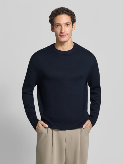 Männermodel trägt Pullover mit Rippbündchen von Selected Homme in Dunkelblau, Feinstrick, unifarben, Rundhals, Ganzkörperansicht von vorne.