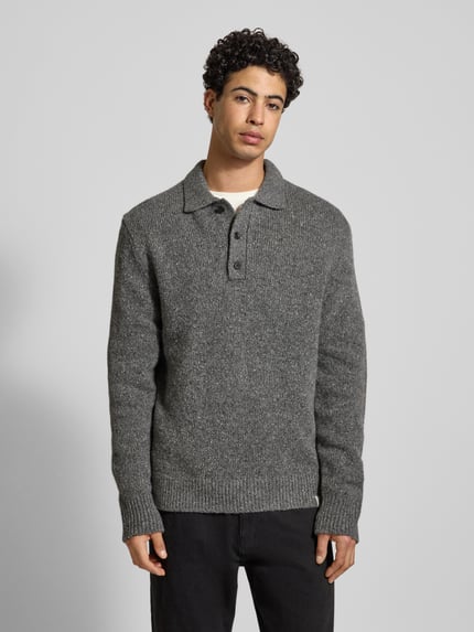 Männermodel trägt Strickpullover aus Woll-Mix mit Polokragen von Calvin Klein Jeans in Grau, Regular-Fit, Knopfleiste, Label-Detail, Ganzkörperansicht von vorne. Rückenlänge bei Größe M 76 cm, Ärmellänge 72 cm.