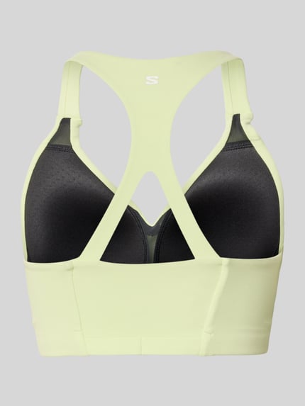 Vrouwenmodel draagt Racerback-Bustier met Logo van Salomon, lichte kleur, aansluitende pasvorm, stretchmateriaal, logo, racerback. Ganzkörperansicht Rückansicht.