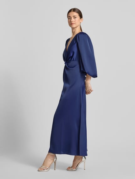 Frauenmodel trägt Maxikleid mit Ballonärmeln Modell 'THEA' von YAS, Material-Mix mit Stretch-Anteil, taillierter Schnitt, V-Ausschnitt, Knoten-Detail, in kräftigem Dunkelblau, glatte Textur, Ganzkörperansicht von vorne.