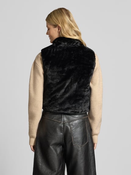 Frauenmodel trägt Regular Fit Weste mit Wende-Funtion Modell 'DANA' von ONLY in Schwarz auf beigefarbenem Pullover, Damen Weste, Ganzkörperansicht Rückansicht.