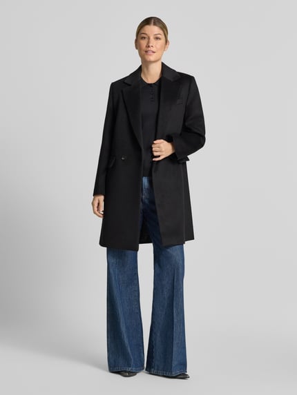 Frauenmodel trägt schwarzen Regular Fit Mantel mit Reverskragen Modell 'DALI' von MANGO, Zwei-Knopfleiste, Ganzkörperansicht von vorne. Rückenlänge 93 cm, Schulterbreite 38 cm, Brustweite 47 cm, Ärmellänge 60 cm.