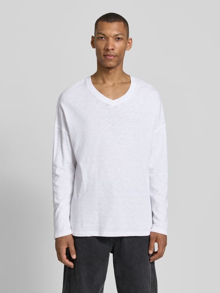 Männermodel trägt Longsleeve mit überschnittenen Schultern Modell 'SONOMA' von American Vintage in Weiß, reine Baumwolle, V-Ausschnitt, Ganzkörperansicht von vorne.