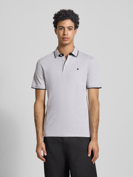 Męski model nosi koszulkę polo Slim Fit Poloshirt mit Viskose-Anteil Modell 'Paulos' od JACK & JONES, mieszanka bawełny i wiskozy, krój slim fit, kołnierzyk polo, krótki rękaw, wyhaftowane logo, długość tyłu w rozmiarze M: 72 cm, widok całej sylwetki z przodu.