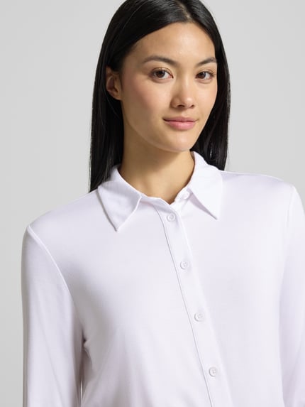 Frauenmodel trägt weiße Slim Fit Hemdbluse aus Viskose-Mix von COMMA mit Knopfleiste und Hemdblusenkragen, Nahaufnahme Oberkörper.