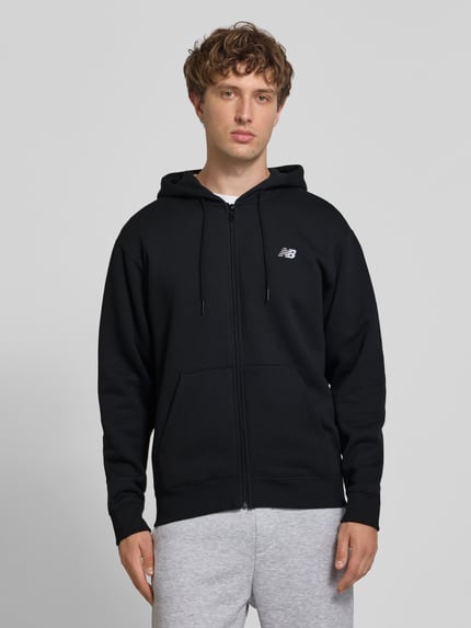 Männermodel trägt Sweatjacke mit Känguru-Tasche und Label-Stitching von New Balance, schwarz, Baumwoll-Mix, Ganzkörperansicht von vorne