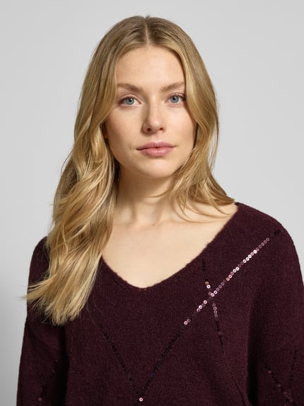 Frauenmodel trägt Strickpullover mit Paillettenbesatz von Milano Italy in Dunkellila, lockerer Schnitt, U-Ausschnitt, Material-Mix, Nahaufnahme Oberkörper.