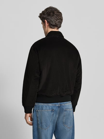 Männermodel trägt schwarze Bomberjacke mit Cordstruktur von LACOSTE, unifarben, Logo-Patch, gerippt, Ganzkörperansicht Rückansicht.