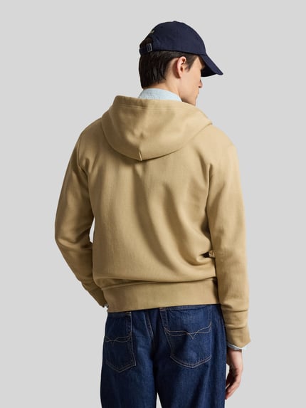 Męski model nosi Regular Fit Sweatjacke aus Baumwoll-Mix von Polo Ralph Lauren w kolorze beżowym, proste formy, tekstura gładka, widok całej sylwetki od tyłu.