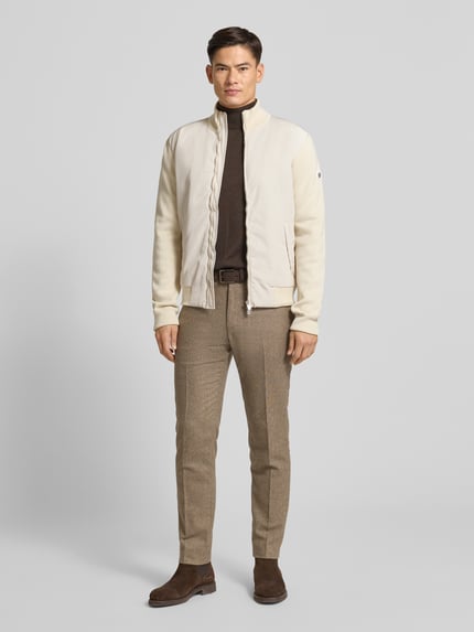 Männermodel trägt Regular Fit Strickjacke aus reiner Baumwolle Modell 'IBAIO' von BOSS in Beige mit Zweiwege-Reißverschluss, Ganzkörperansicht von vorne.