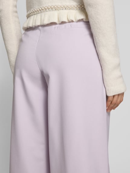 Kobiece modelka nosi Wide Fit Stoffhose mit Bundfalten Modell 'Kate' od Guido Maria Kretschmer, liliowy kolor, gładka faktura, detal tylnej części, długość wewnętrzna nogawki 78 cm, szerokość w rozmiarze 36: 36 cm, zapięcie na haftkę i zamek błyskawiczny, spodnie materiałowe, zakładki w pasie, model dla kobiet, detaliczny widok tylnej części.