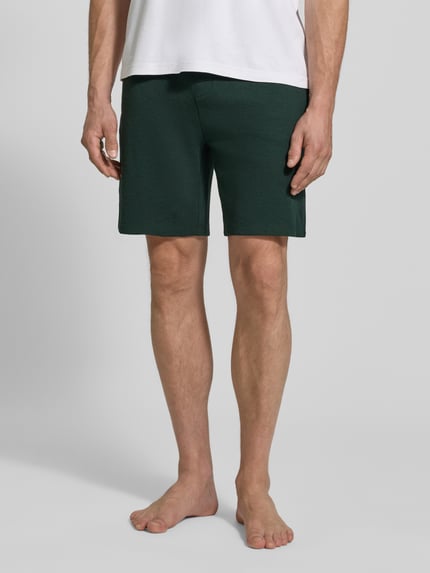 Männermodel trägt Sweatshorts mit Waffelstruktur von BOSS in Dunkelgrün, Baumwollmix, seitliche und Gesäßtaschen, Ganzkörperansicht von vorne.