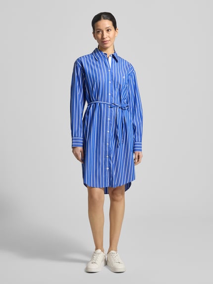 Frauenmodel trägt knielanges Hemdblusenkleid mit Bindegürtel von Gant in Blau mit weißen Streifen, reine Baumwolle, gerader Schnitt; Ganzkörperansicht von vorne.